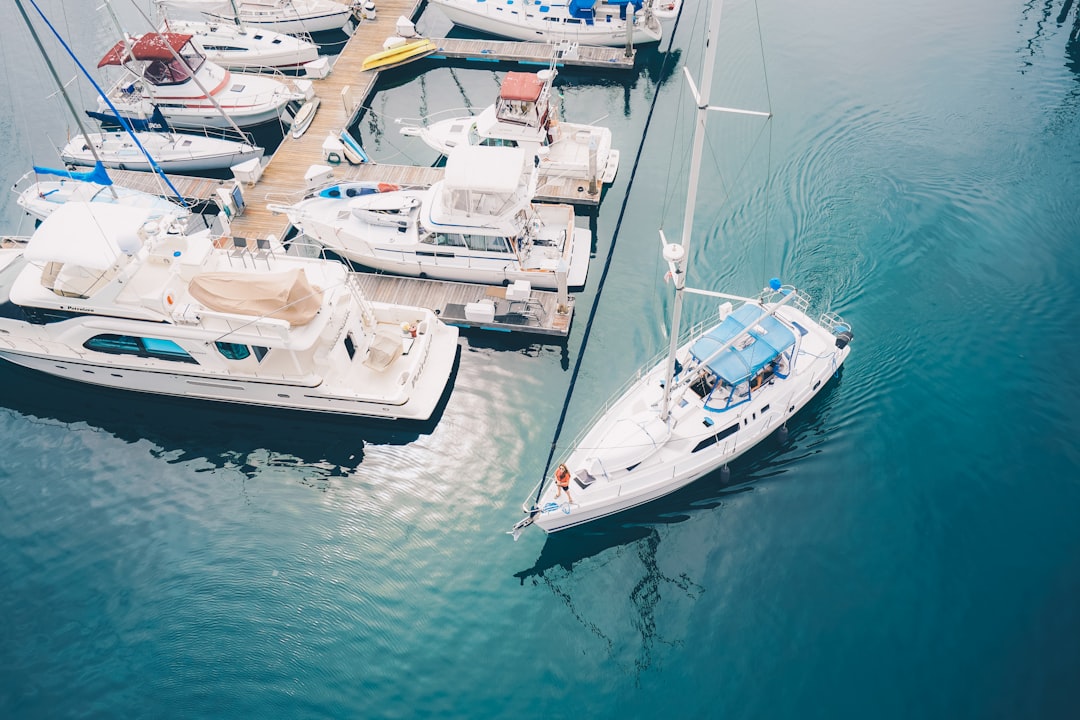 A person inspecting a boat in a marina, preparing it for the boating season with tools and maintenance equipment nearby.